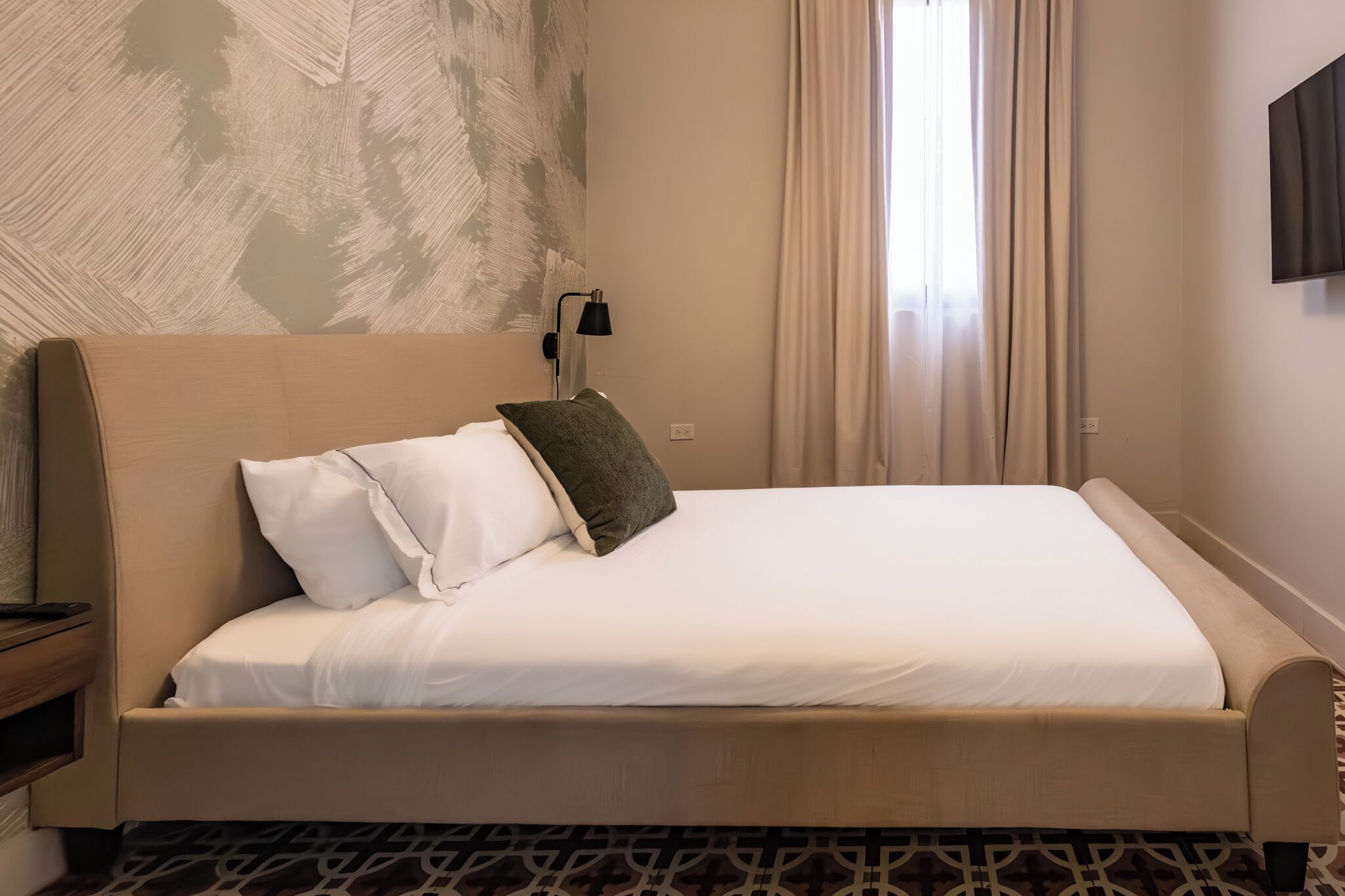 A neatly made bed with white and green pillows, a bedside lamp, and a patterned carpet.
