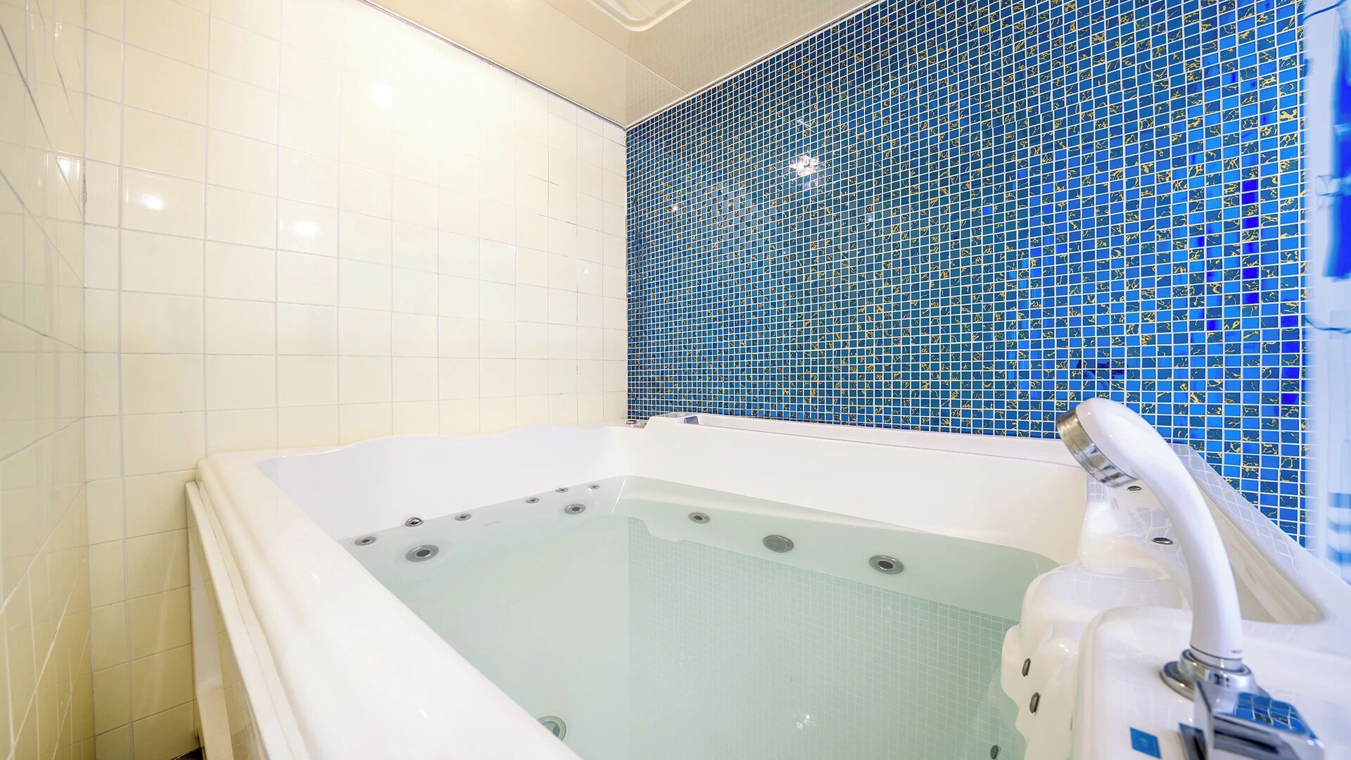 A modern bathroom with a glass-enclosed bathtub, white tiles, and a blue mosaic wall.