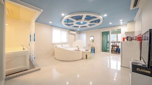 A modern bedroom with a curved bed, a ceiling with a circular design, and a bathroom with a white tub.