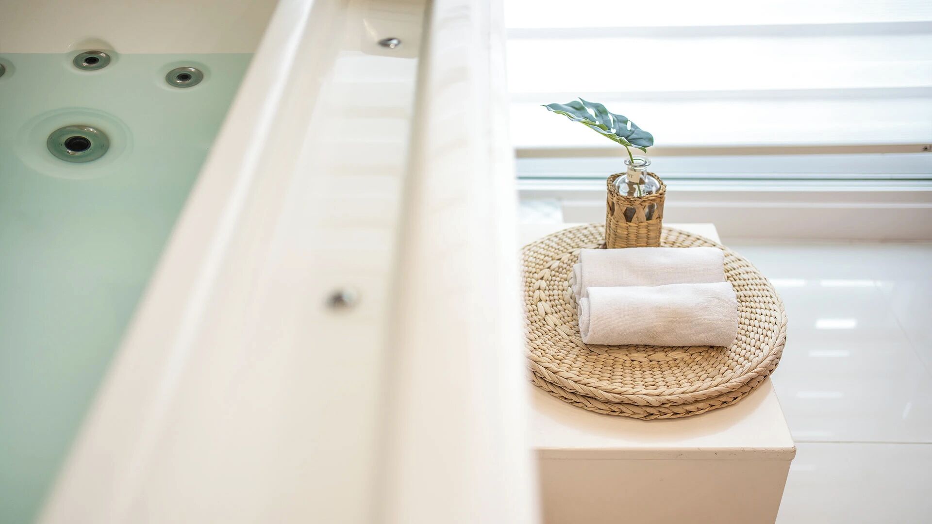 A spa tub with a woven mat and towels on a white pedestal.