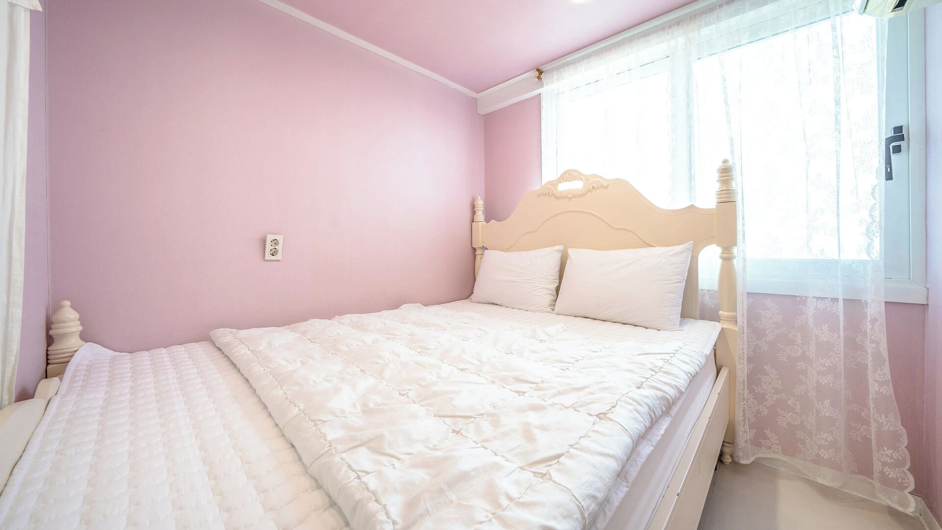 Un dormitorio con una cama individual, cabecera y ventana con cortinas translúcidas.