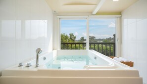 A modern bathroom with a large bathtub, a window with a view of greenery, and a balcony. - Gyeongju Nunkoip Pension (Gyeongju)