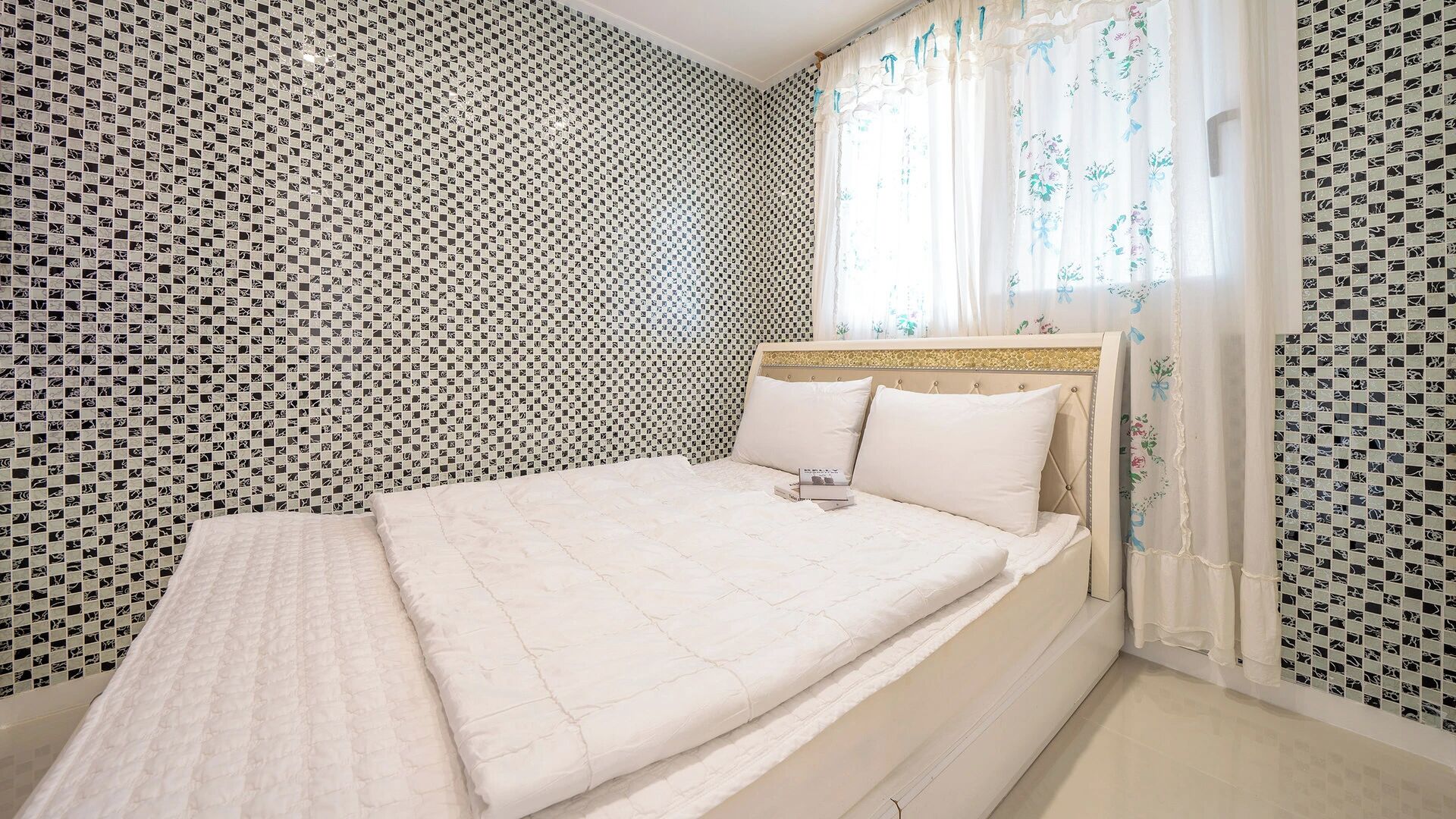 Une chambre à coucher avec un lit, une tête de lit et une fenêtre avec des rideaux.