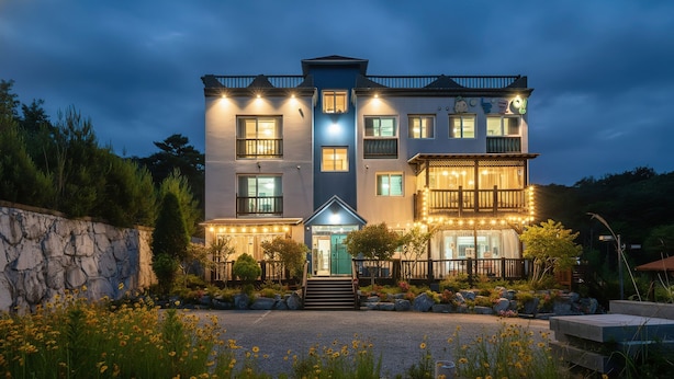 A multi-story building with a stone wall, a well-lit entrance, and a balcony with string lights. - Gyeongju Nunkoip Pension (Gyeongju)
