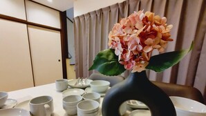 Una mesa de comedor con un jarrón negro que contiene flores rosas, rodeada de cuencos y tazas blancos.