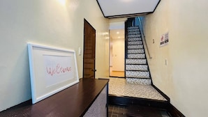 Un área de recepción con un cartel de bienvenida enmarco, un mostrador de recepción oscuro y una escalera que conduce a un piso superior.