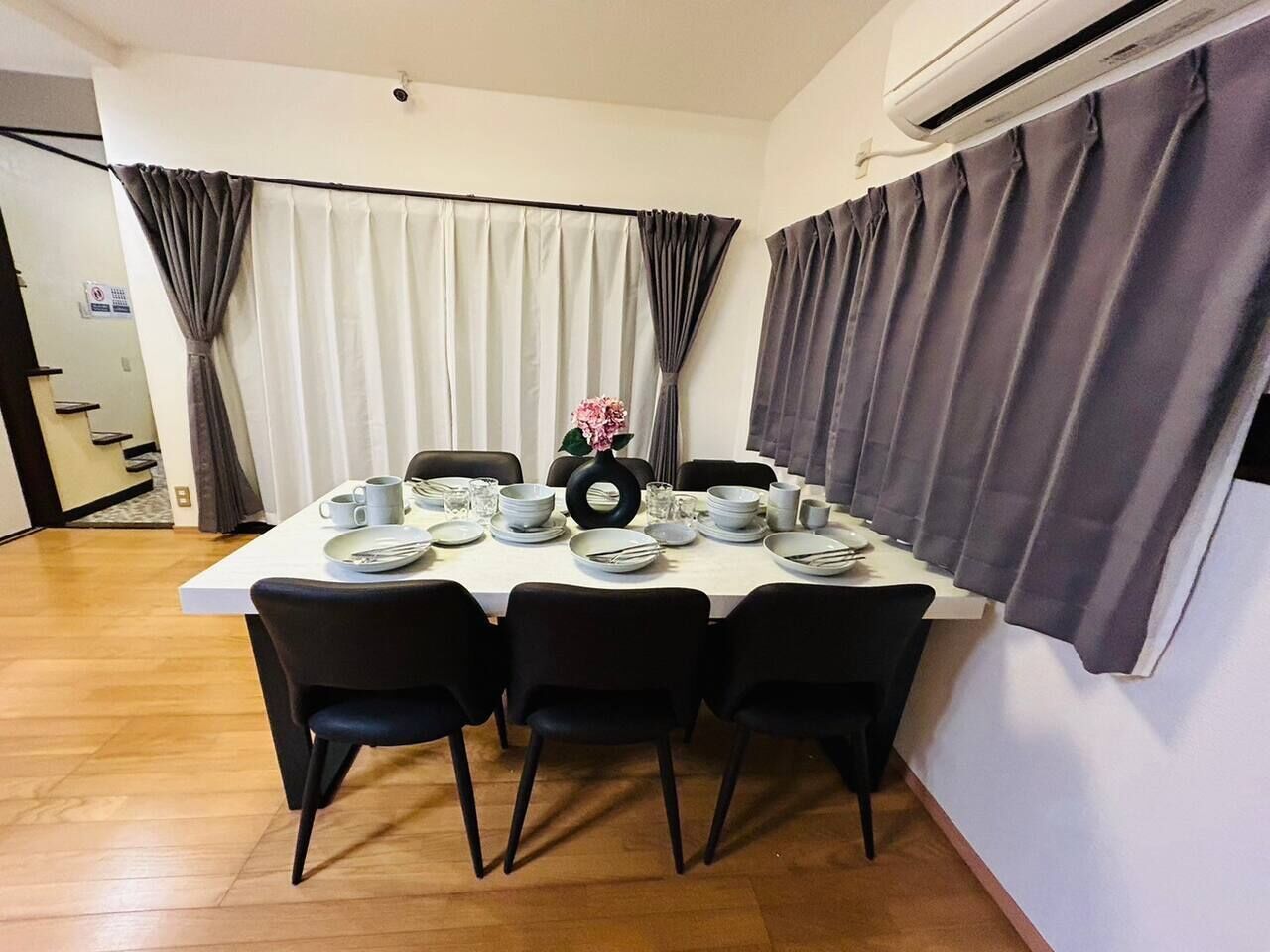 A dining area with a table set for four, chairs, a vase with flowers, and a window with curtains.