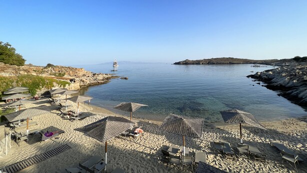 A beach with umbrellas, lounge chairs, and a rocky shoreline. - Sandy Side Mykonos by Angels Group (Mykonos)
