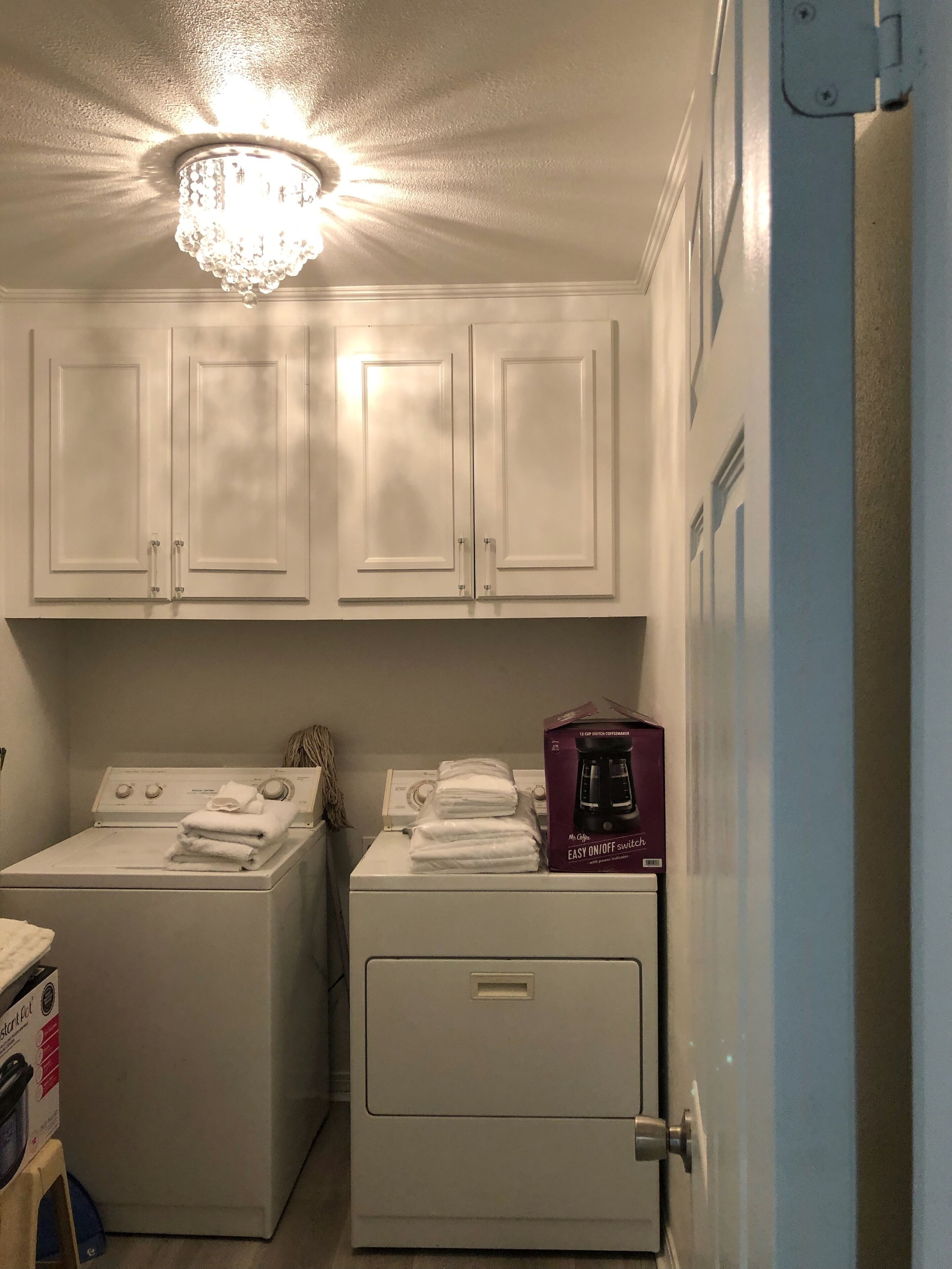 A laundry room with two washing machines, a dryer, and a coffee maker on top of the dryer.