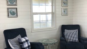 Ein Zimmer mit zwei dunkelblauen Sesseln, einem kleinen Glastisch und einem Fenster mit weißen Fensterläden.