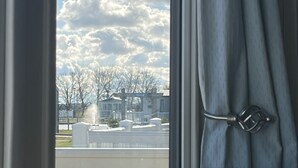 A view through a window with curtains, featuring a residential area with houses and trees. - The Lakes Escape Haven Golden Sands Mablethorpe (Mablethorpe)