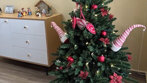 Un árbol de Navidad con adornos rojos y decoraciones de bastones de caramelo en una habitación con piso de madera y un aparador blanco.