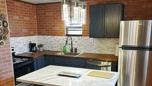 Cocina compacta con isla central, refrigerador de acero inoxidable y un salpicadero de ladrillo.