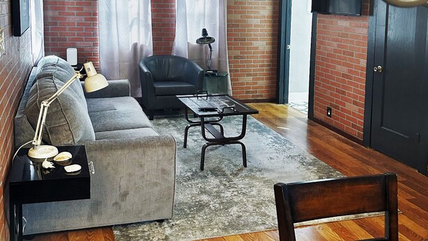 Una sala de estar con un sofá, una mesa de centro, una silla y un televisor montado en la pared.