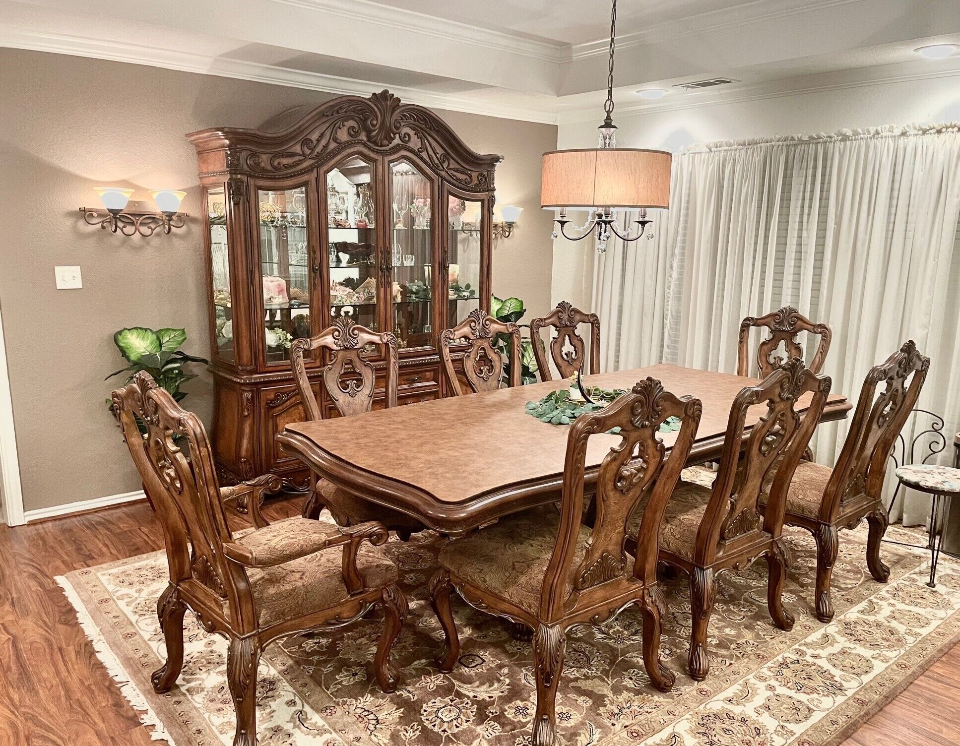 Une salle à manger avec une grande table en bois, des chaises décorées, un meuble avec des miroirs et un lustre.