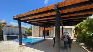 Un espacio exterior cubierto con piscina, un patio con sillas y un edificio de fachada con azulejos.