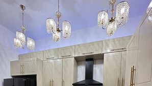 Una cocina moderna con armarios de colores claros, un refrigerador negro, una estufa y una lámpara de araña.