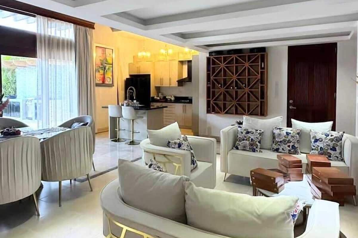 A spacious living area with a modern sofa set, a dining table, and a kitchen in the background.
