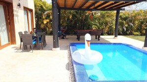 Una piscina con un flotador con forma de cisne, rodeada de mobiliario exterior y palmeras.