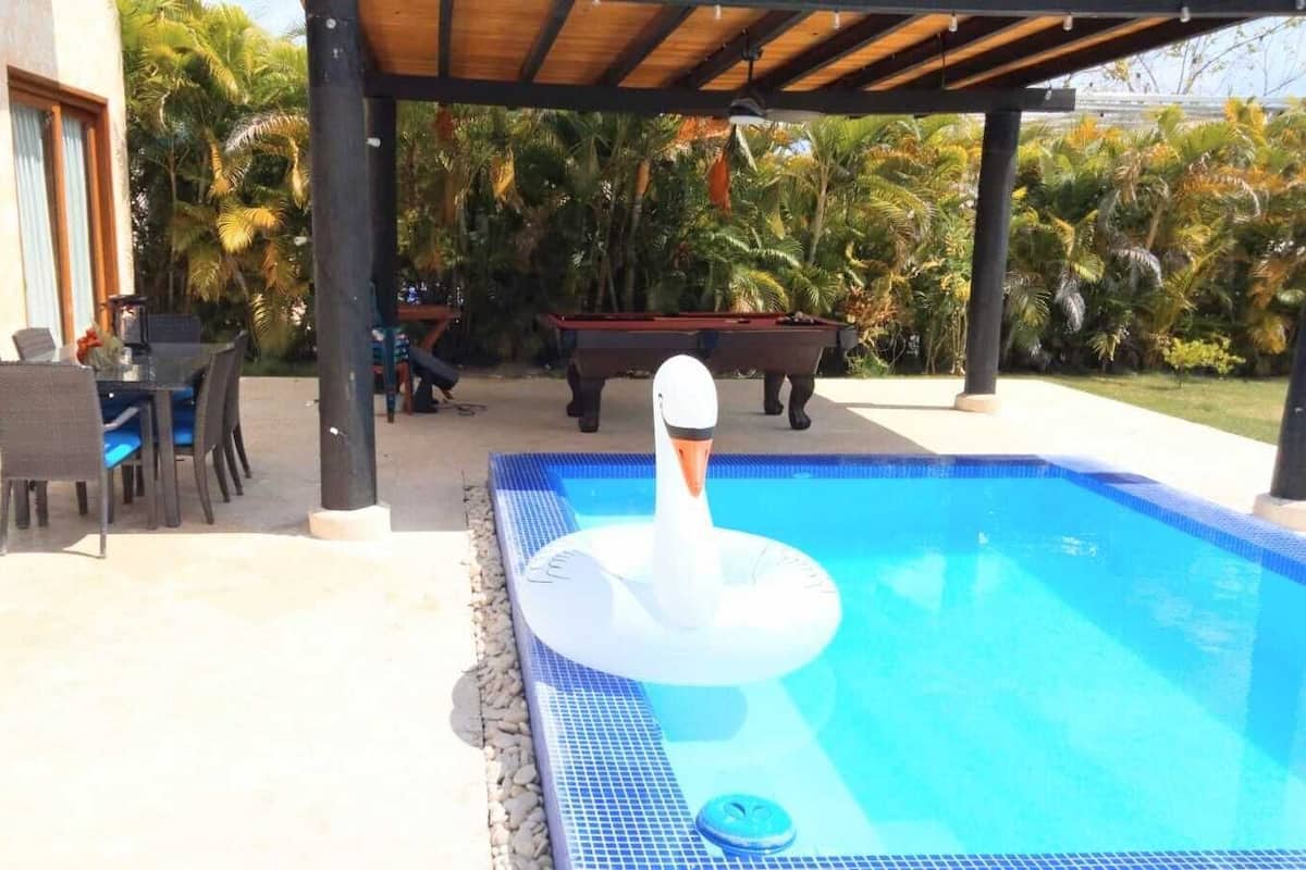 A swimming pool with a swan float, surrounded by outdoor furniture and palm trees.