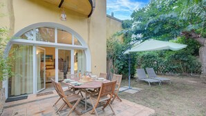 An outdoor patio with a wooden table and chairs, a covered seating area, and a view of the interior through a glass door. - Villa Azzurra Front Beach - Pool, Gassin, France (Gassin)