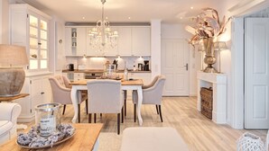 Een moderne keuken met witte kasten, een eethoek met een houten tafel en stoelen, en een kroonluchter.