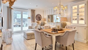 Een ruime eethoek met een houten tafel, gestoffeerde stoelen en een kroonluchter.
