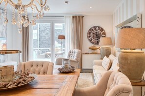 Un salon spacieux avec une grande table en bois, des fauteuils confortables, un lustre et une grande horloge murale.