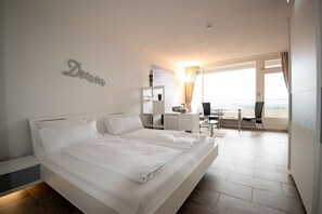 Une chambre d’hôtel moderne, dotée d’un grand lit, d’un bureau et d’une chaise. Elle dispose également d’un balcon avec vue.