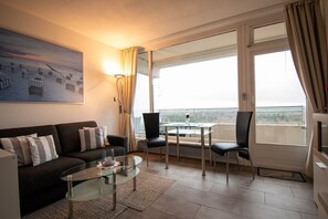 Une chambre d’hôtel moderne dotée d’un balcon, d’un canapé, d’une table basse en verre et d’un coin repas avec des chaises.