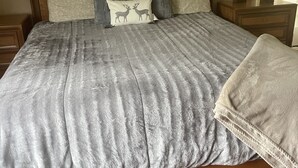 Een groot bed met een grijs geweven sprei, een houten hoofdbord en een grijze plaid.