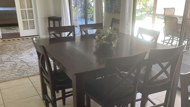Een eethoek met een grote houten tafel en stoelen, een vaas met bloemen, en uitzicht op het buitengebied door grote ramen.