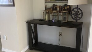 Een kamer met een donker houten consoletafel, een lamp en een plank met boeken en decoratieve voorwerpen.