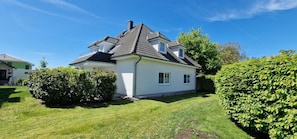 Une maison à deux étages, dotée d’un toit en pente, d’un petit garage attenant et d’une pelouse bien entretenue.