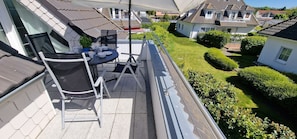 Un balcon avec une table et des chaises, donnant sur un jardin bien entretenu et les maisons voisines.