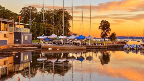 A marina with boats docked, a building labeled "Sailing Club," and a calm water body reflecting the surroundings. - Sailors Cove | Pet Friendly (Point Frederick)