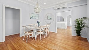 A dining area with a round table, white chairs, a chandelier, and a potted plant. - Sailors Cove | Pet Friendly (Point Frederick)
