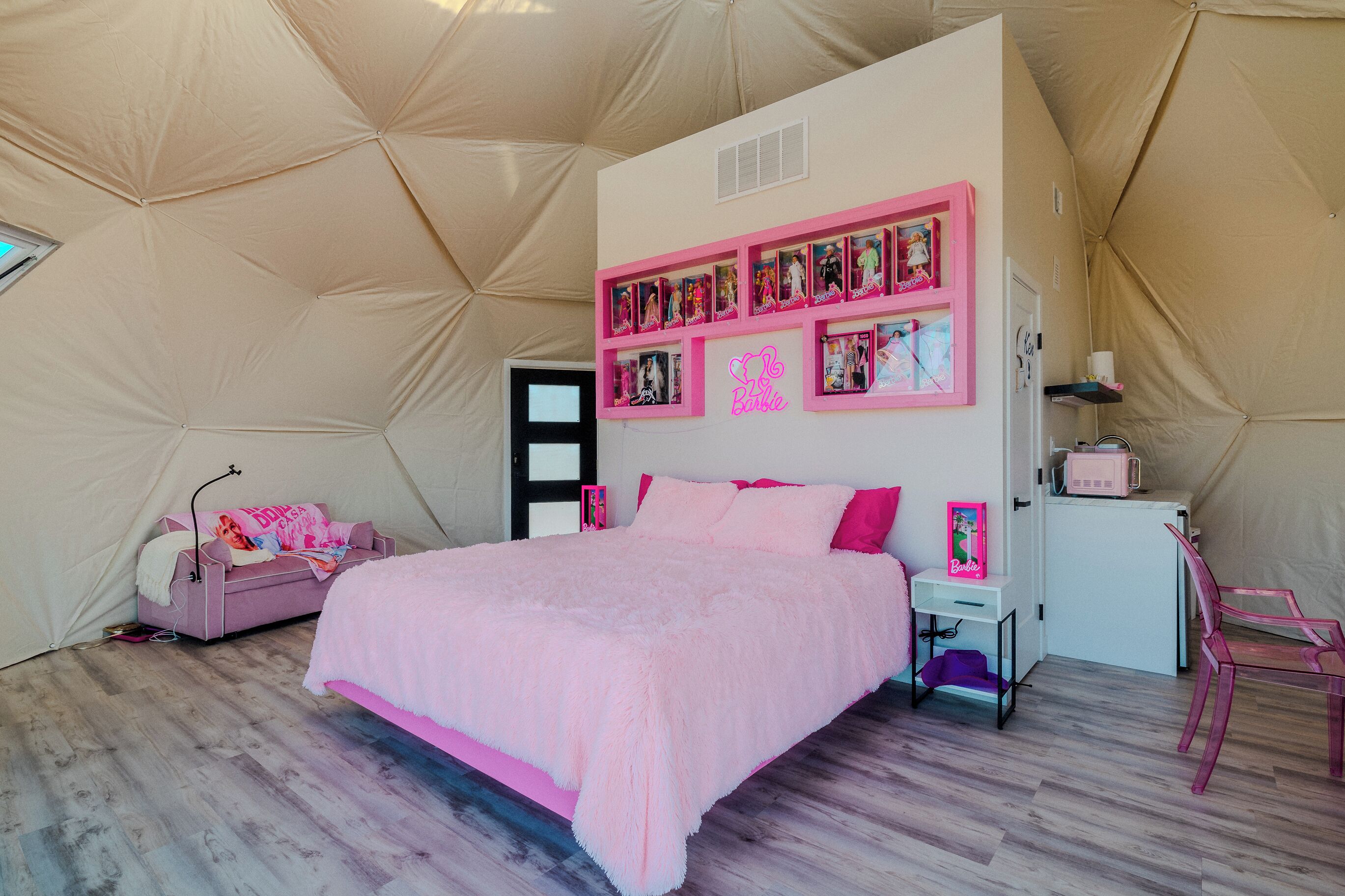 Une pièce aménagée comme une tente, avec un lit, une décoration aux tons rose et blanc, et une étagère ornée de cadres avec des photos.
