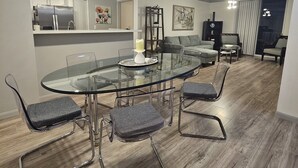 Ein moderner Essbereich mit Glastisch und Metallstühlen, im Hintergrund eine Küche und ein Wohnbereich mit Sofa und Couchtisch.