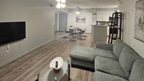 Ein modernes Wohnzimmer mit grauem Sofa, einem Glastisch und einem an der Wand montierten Flachbildfernseher.