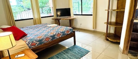 A bedroom with a bed, a TV, a wooden shelf, and a window with curtains.