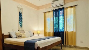 A bedroom with a wooden bed, a wall-mounted air conditioner, and a window with yellow and blue curtains. - Beautiful Carillo poolside condo w/ AC! Location+ (Puerto Carrillo)