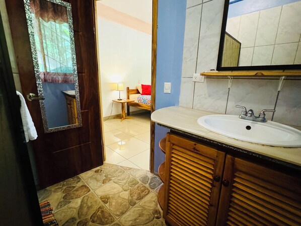 A bathroom with a wooden vanity, a sink, and a mirror. There is a door leading to another room. - Beautiful Carillo poolside condo w/ AC! Location+ (Puerto Carrillo)
