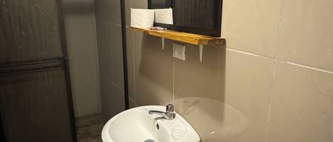Un baño con lavamanos blanco, espejo superior y zona de ducha.