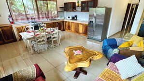 A modern kitchen with wooden cabinets, a stainless steel refrigerator, and a dining area with a white table and chairs. - Beautiful Carillo poolside condo w/ AC! Location+ (Puerto Carrillo)