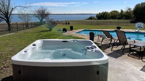 Un bain à remous avec vue sur un lac, entouré d’une terrasse dotée de chaises et d’une piscine.