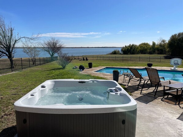A hot tub with a view of a lake, surrounded by a deck with chairs and a pool. - Luxury Lake House with Pool table & Hot Tub (Lakewood Village)