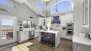 Une cuisine moderne avec des meubles blancs, un îlot central doté de tabourets, une grande fenêtre et une vue sur l’extérieur.