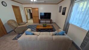 Una sala de estar con sofá, sillón reclinable, una mesa de centro, televisor y ventana con cortinas.