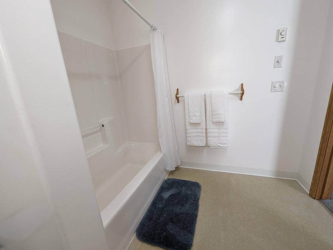 Un baño con bañera, cortina de ducha, toallero con toallas y un tapete azul oscuro en el suelo.